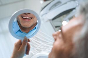 man is looking at mirror and enjoying reflectiong of his smile after dental procedures