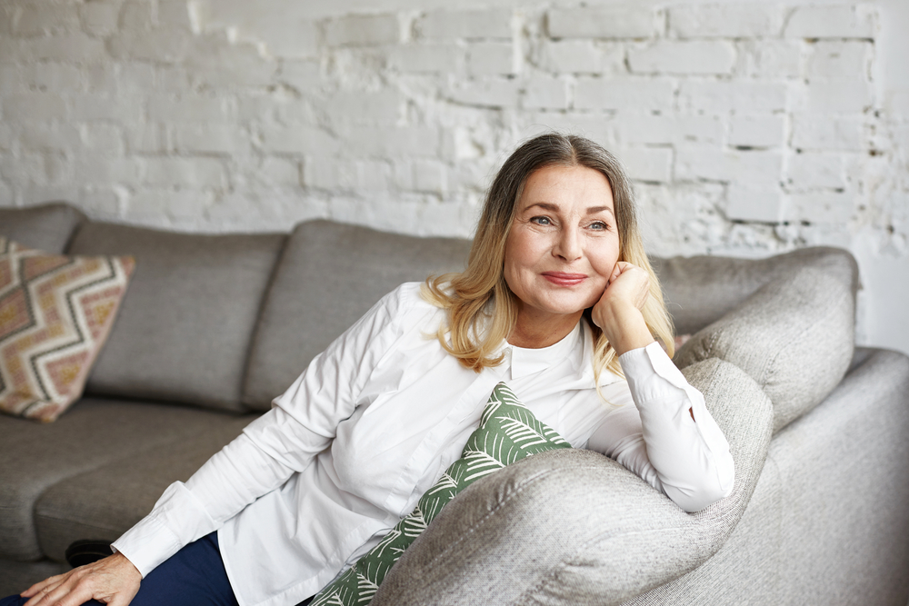 senior woman with pleasant smile relaxing on grey sofa